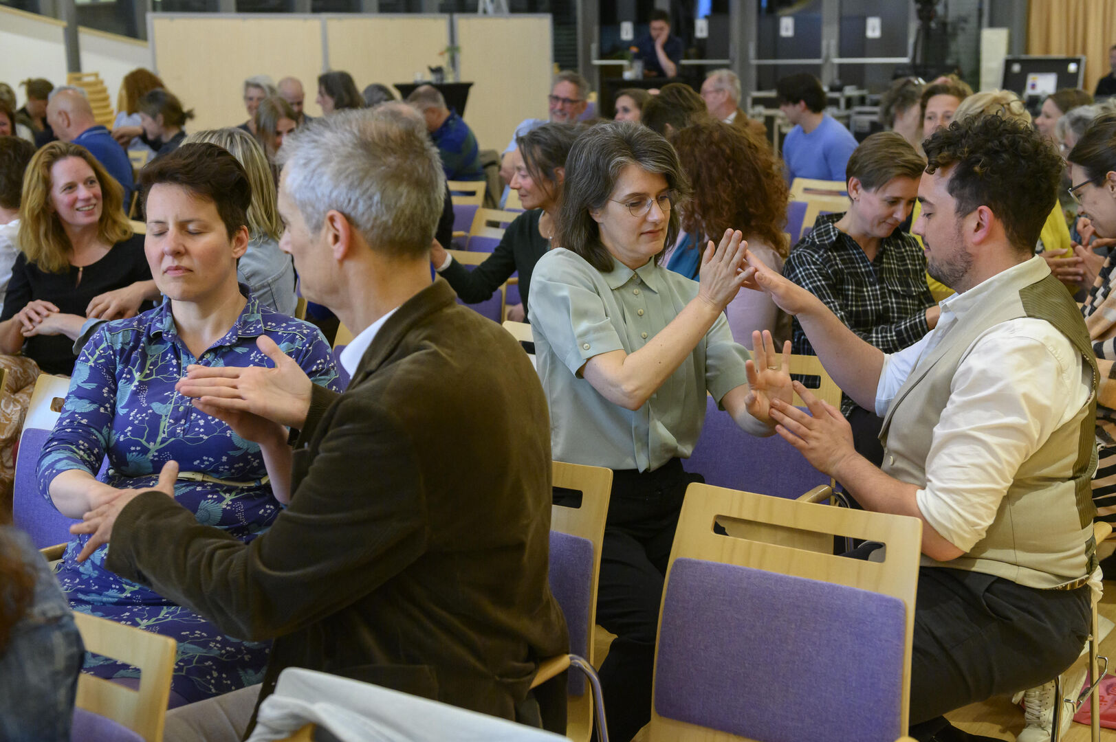 Publiek in tweetallen met ogen dicht en handen tegen elkaar